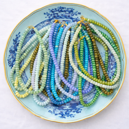 Colorful beaded necklaces on a decorative plate with blue floral patterns