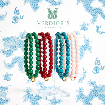 Jewelry display with beaded bracelets in green, red, and blue on a Verdigris Collection stand against a decorative background.