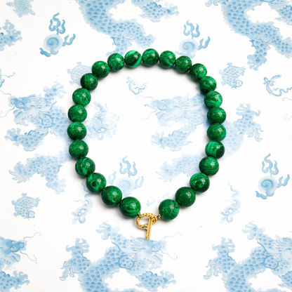 Green beaded bracelet with a gold clasp on a blue patterned background