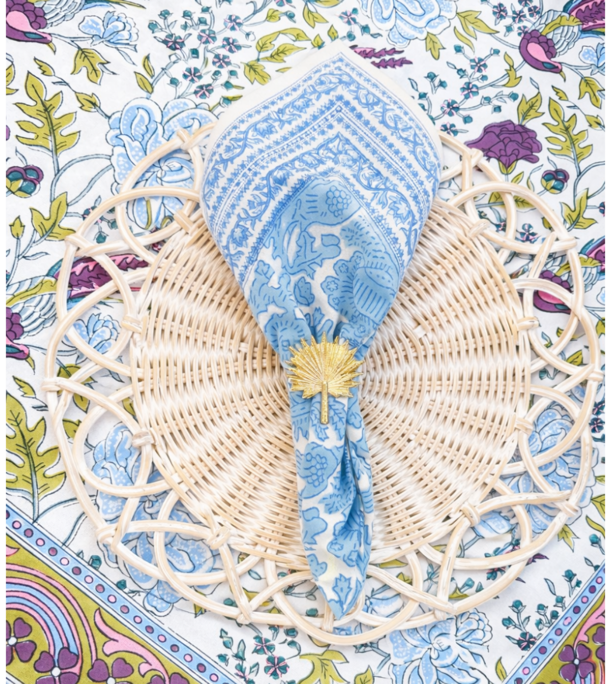 Decorative table setting with a woven placemat and blue fabric on a floral-patterned tablecloth.